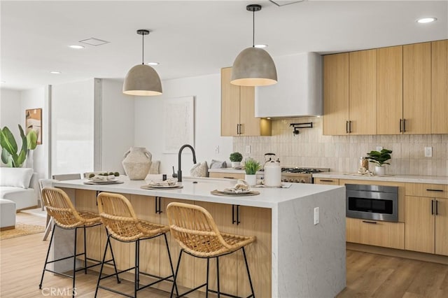 kitchen featuring decorative backsplash, light brown cabinetry, a kitchen breakfast bar, light countertops, and a sink
