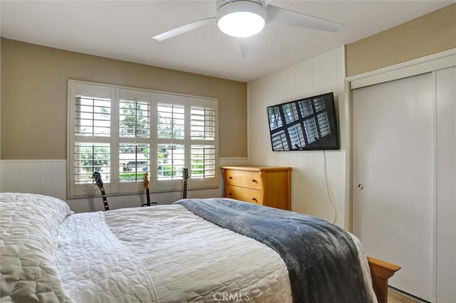 bedroom with wainscoting, a ceiling fan, multiple windows, and a closet