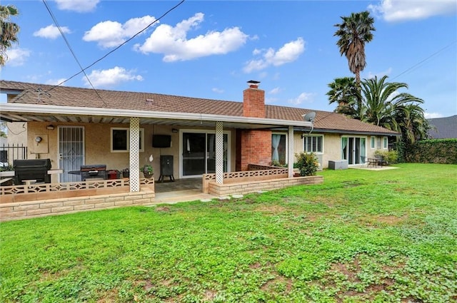 rear view of house featuring a patio area, a lawn, a chimney, and stucco siding