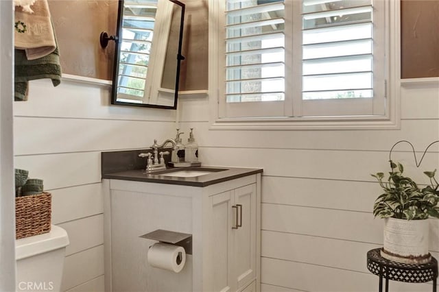 half bath featuring a wealth of natural light, toilet, and vanity