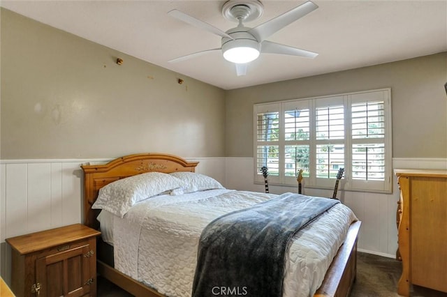 bedroom with wainscoting, a ceiling fan, and dark carpet