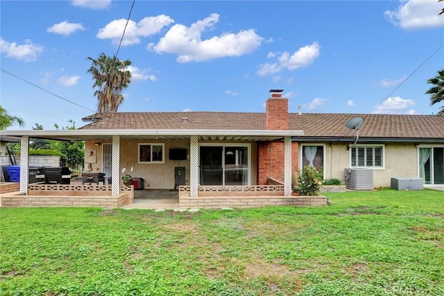 back of house with stucco siding, a chimney, a yard, and a patio