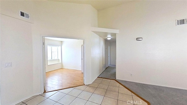 unfurnished room with baseboards, light tile patterned floors, a towering ceiling, and visible vents