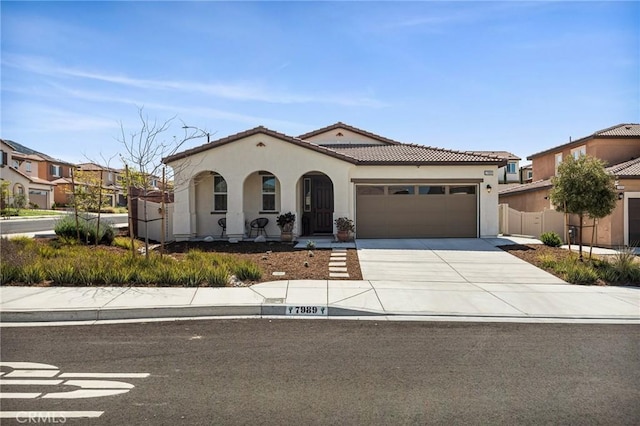 mediterranean / spanish home with a tiled roof, stucco siding, fence, a garage, and concrete driveway