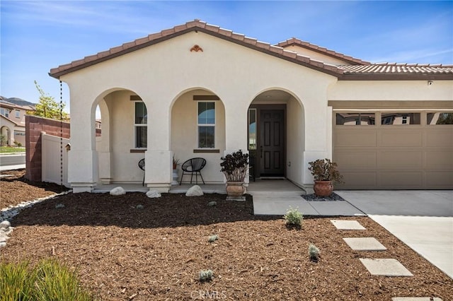 mediterranean / spanish-style home with a porch, a garage, a tile roof, concrete driveway, and stucco siding