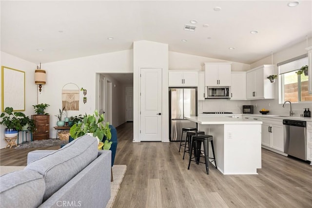 kitchen featuring a kitchen breakfast bar, vaulted ceiling, open floor plan, a kitchen island, and appliances with stainless steel finishes