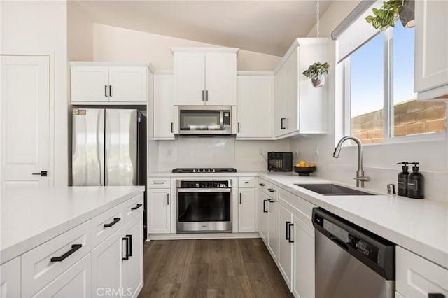 kitchen featuring dark wood finished floors, white cabinets, appliances with stainless steel finishes, a sink, and lofted ceiling