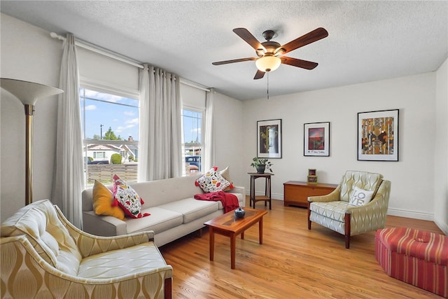 living area featuring light wood finished floors, a textured ceiling, a ceiling fan, and baseboards