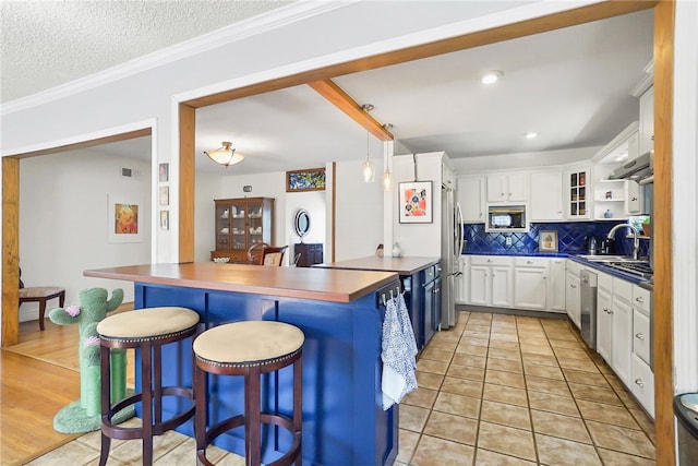 kitchen featuring white cabinets, a kitchen breakfast bar, backsplash, light tile patterned floors, and appliances with stainless steel finishes