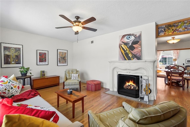 living area featuring a fireplace with flush hearth, a textured ceiling, ceiling fan, visible vents, and wood finished floors