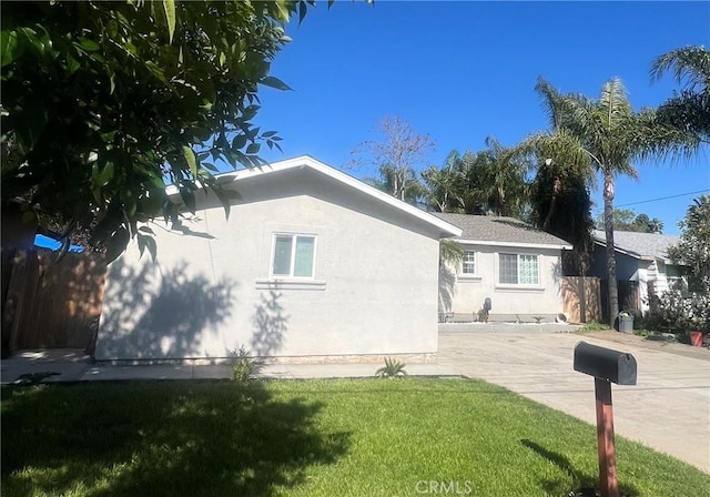 view of side of home featuring a yard, fence, and stucco siding