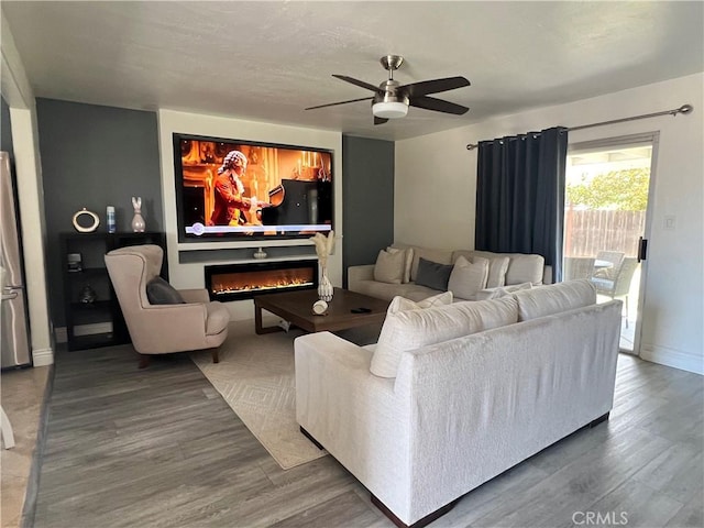 living room featuring wood finished floors, baseboards, a ceiling fan, and a glass covered fireplace