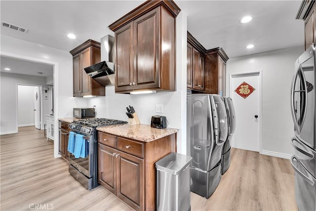 kitchen featuring stainless steel appliances, light stone countertops, light wood-style flooring, and wall chimney range hood