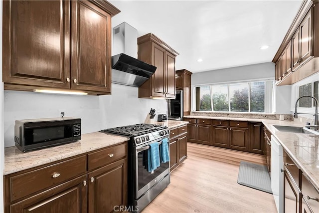 kitchen featuring black microwave, wall chimney exhaust hood, light wood finished floors, stainless steel gas stove, and a sink