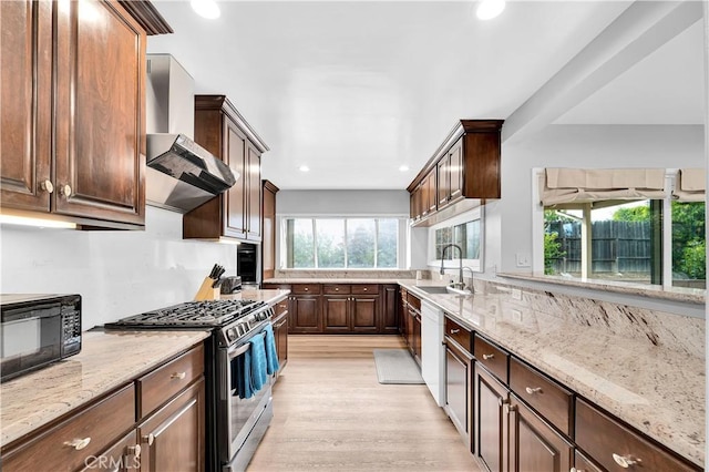 kitchen featuring black microwave, wall chimney range hood, light stone counters, a sink, and stainless steel gas range oven