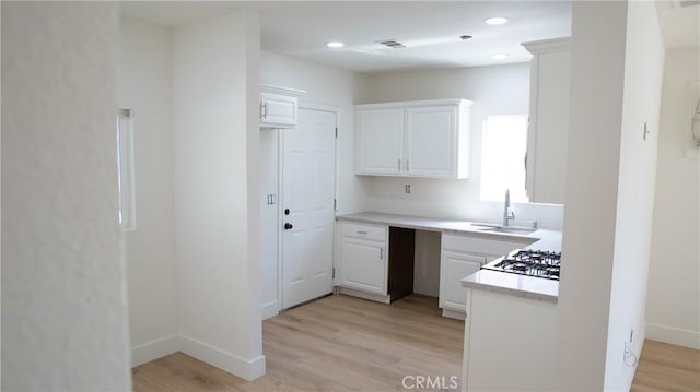 kitchen with white cabinets, a sink, light wood finished floors, light countertops, and visible vents
