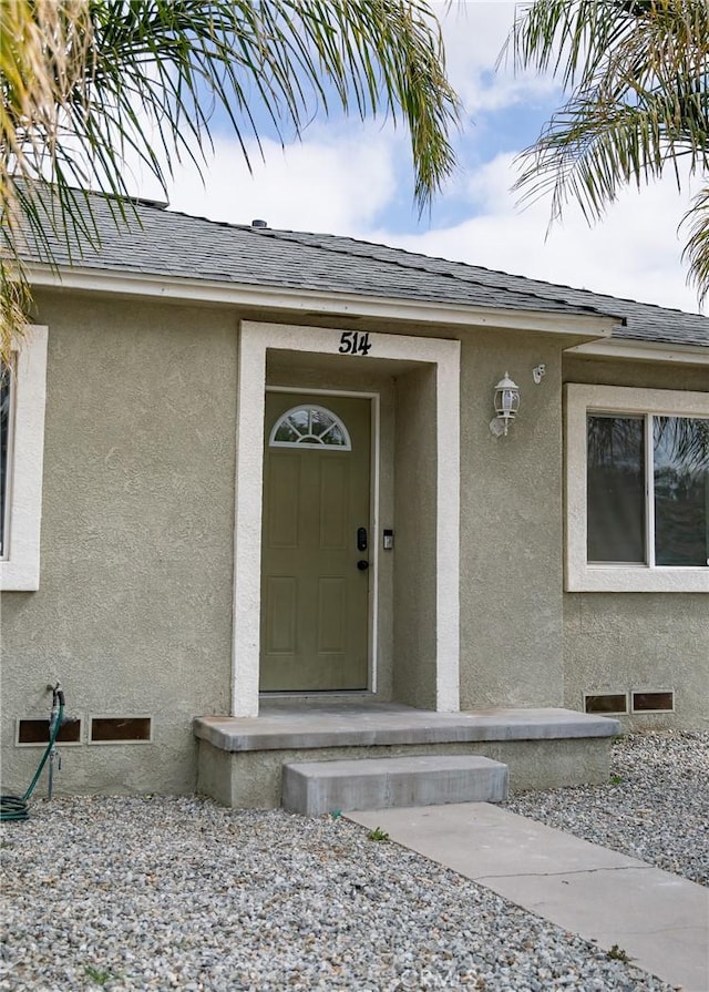 doorway to property featuring a shingled roof and stucco siding