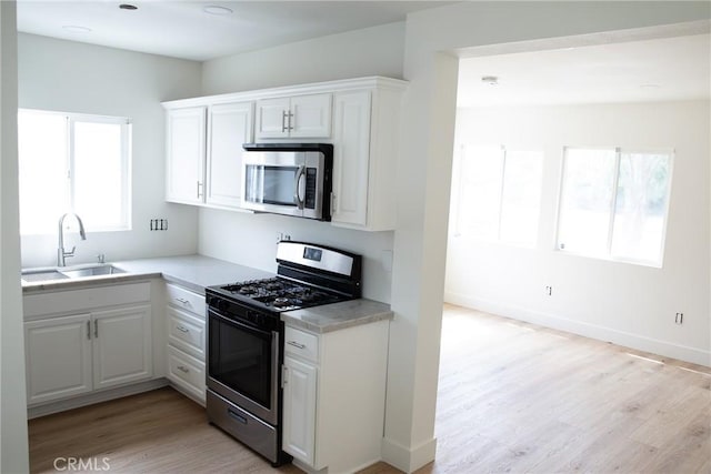 kitchen with light wood-style floors, light countertops, white cabinetry, a sink, and stainless steel appliances
