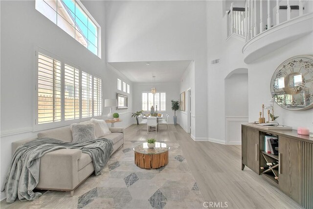 living room featuring visible vents, arched walkways, a high ceiling, light wood-type flooring, and a chandelier