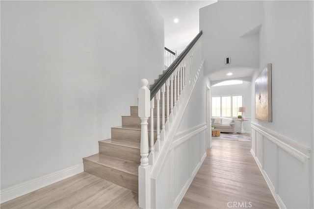 stairway featuring arched walkways, wood finished floors, a high ceiling, and recessed lighting