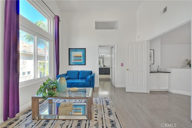 sitting room featuring light wood-style floors, a healthy amount of sunlight, a high ceiling, and visible vents