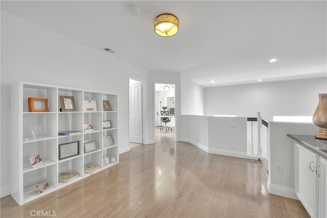 interior space with wood finished floors, baseboards, visible vents, and an upstairs landing