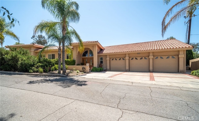 mediterranean / spanish-style house featuring a tiled roof, an attached garage, concrete driveway, and stucco siding