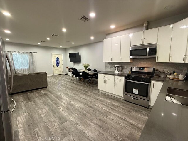 14615 Wyandotte St, Van Nuys, CA 91405 - kitchen with dark countertops, white cabinetry, wood finished floors, stainless steel appliances, and decorative backsplash