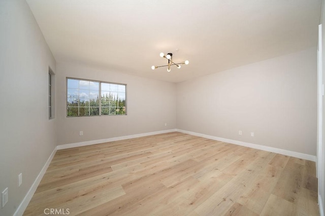 empty room featuring light wood-style flooring, baseboards, and an inviting chandelier