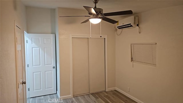 unfurnished bedroom with a closet, baseboards, a ceiling fan, a wall mounted AC, and wood finished floors