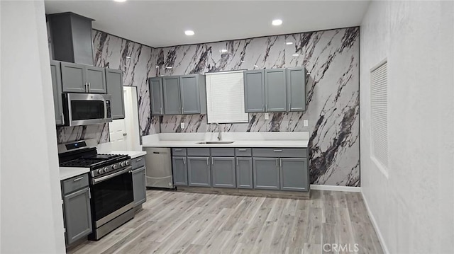 kitchen with gray cabinets, light countertops, a sink, and appliances with stainless steel finishes
