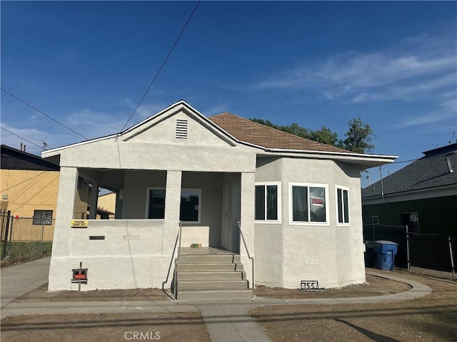 bungalow featuring stucco siding and fence