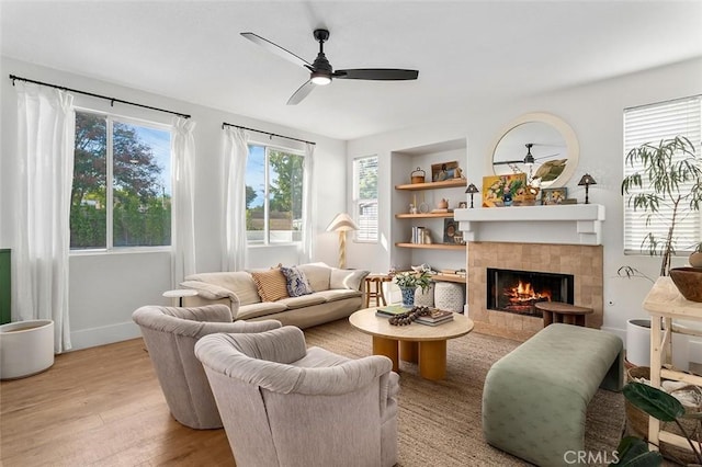 living room with a tiled fireplace, light wood-style floors, and ceiling fan