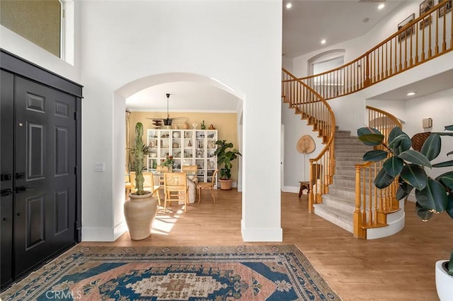 foyer entrance with baseboards, arched walkways, stairway, a towering ceiling, and wood finished floors