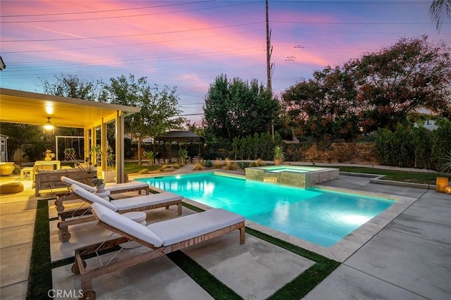 pool at dusk with a patio area and a pool with connected hot tub