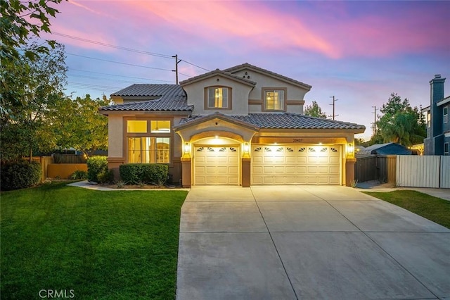 mediterranean / spanish-style home with a tiled roof, concrete driveway, fence, stucco siding, and a front lawn