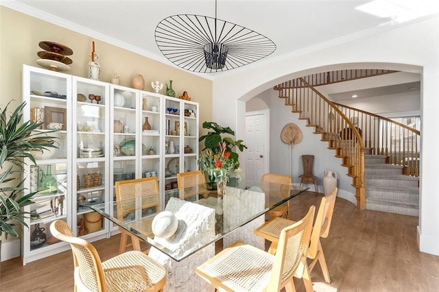 dining room featuring ornamental molding, stairway, arched walkways, and wood finished floors