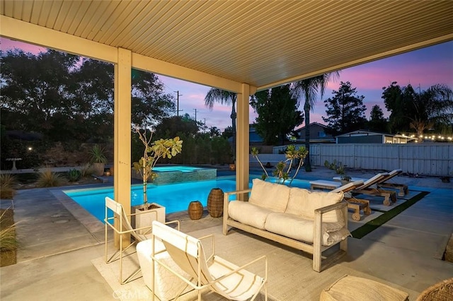 pool at dusk with outdoor lounge area, a patio area, a pool with connected hot tub, and fence