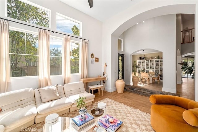 living room featuring a towering ceiling, baseboards, a ceiling fan, arched walkways, and wood finished floors