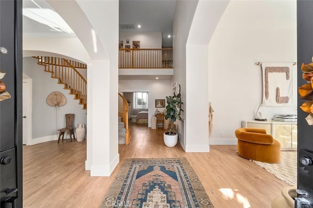 foyer with arched walkways, visible vents, stairs, light wood finished floors, and baseboards