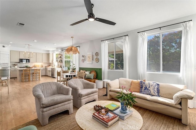 living area featuring visible vents, a wainscoted wall, a ceiling fan, and light wood-style floors
