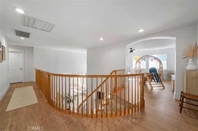 hall featuring arched walkways, visible vents, recessed lighting, wood finished floors, and an upstairs landing