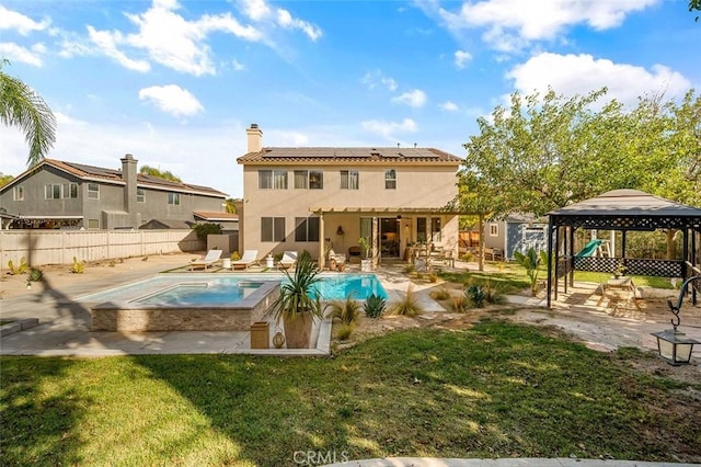 rear view of house with stucco siding, an in ground hot tub, a patio area, solar panels, and a gazebo