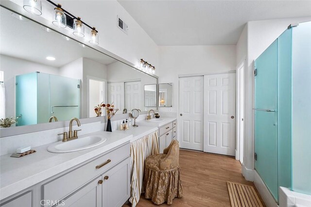 full bath featuring a sink, a shower stall, double vanity, and wood finished floors