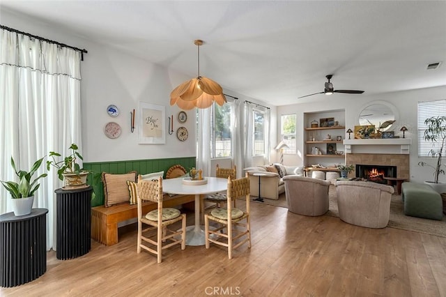 dining room featuring visible vents, a ceiling fan, a wainscoted wall, a fireplace, and light wood-style flooring
