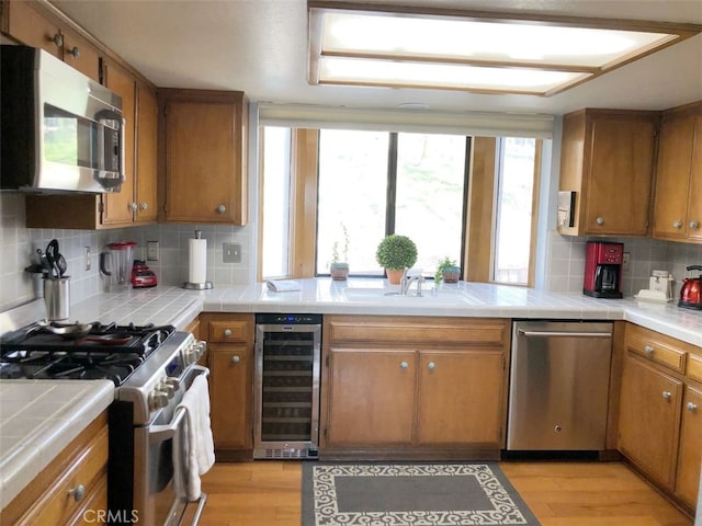 kitchen featuring a sink, appliances with stainless steel finishes, wine cooler, tile counters, and brown cabinets