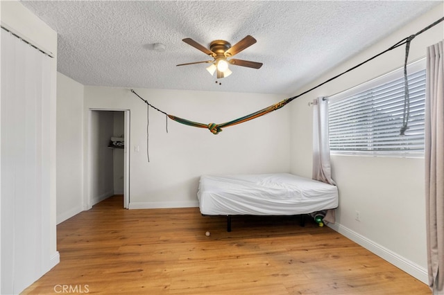 bedroom with light wood-style floors, ceiling fan, baseboards, and a textured ceiling