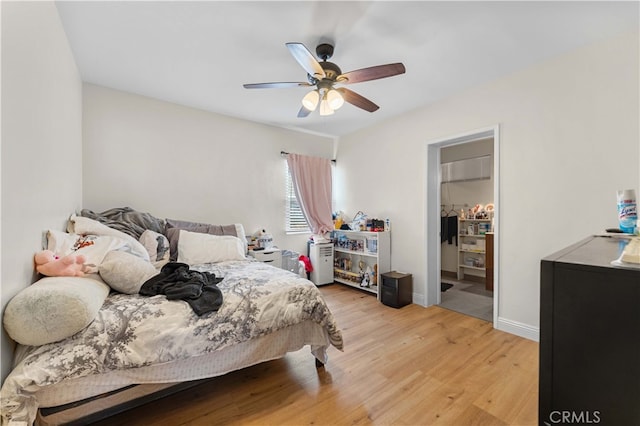 bedroom featuring baseboards, a closet, a spacious closet, ceiling fan, and light wood finished floors