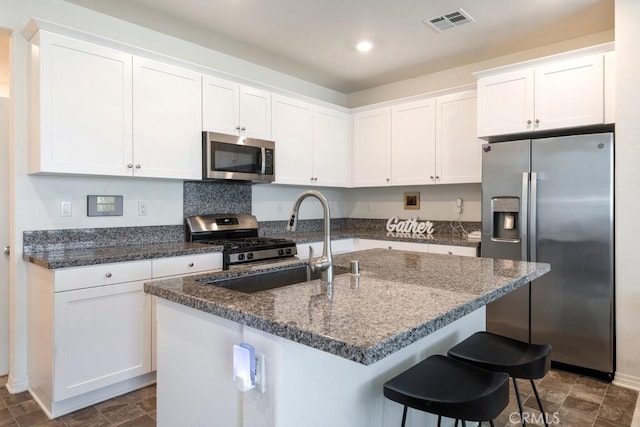 16540 Wyndham Ln Unit 10, Fontana, CA 92336 - kitchen featuring appliances with stainless steel finishes, white cabinets, dark stone counters, an island with sink, and a breakfast bar area