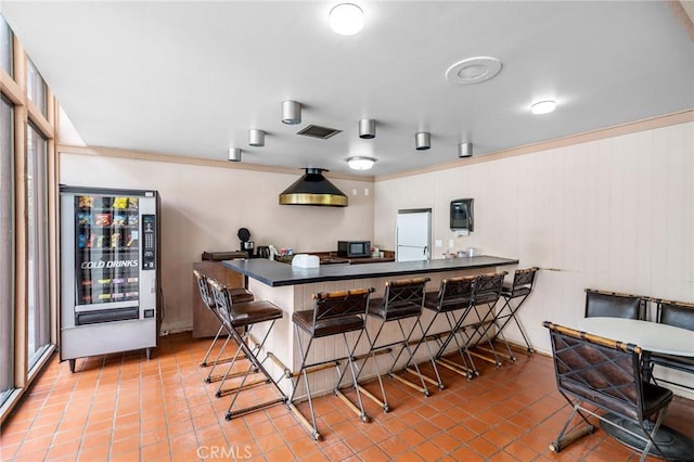 kitchen featuring black microwave, visible vents, dark countertops, tile patterned floors, and a breakfast bar area